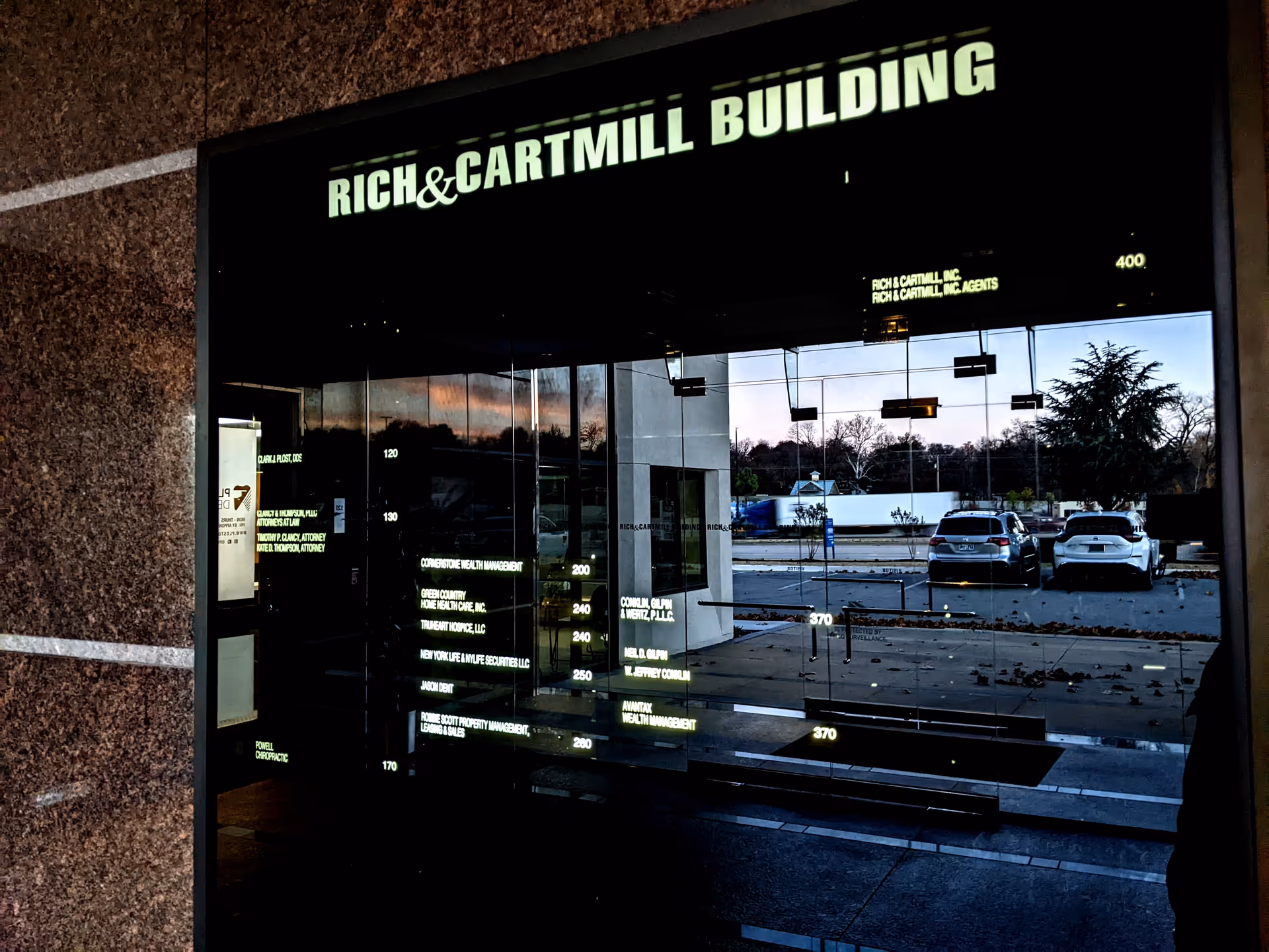 Glass-front building entrance with reflective doors and cars parked outside.
