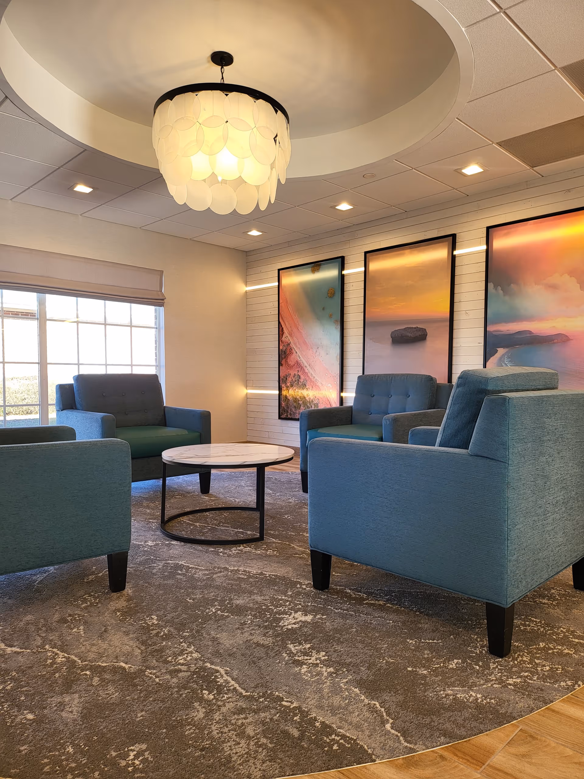 A modern lounge with teal chairs, a round coffee table, and wall art.