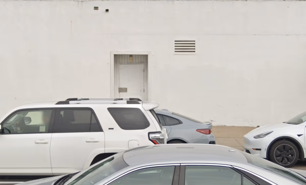 White building exterior with a door and several parked cars in front.