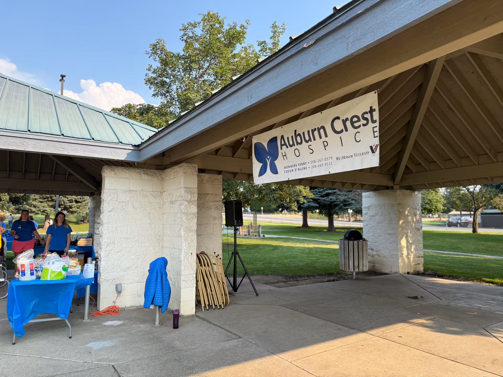 Outdoor pavilion with Auburn Crest Hospice banner and volunteers at a table under shade.