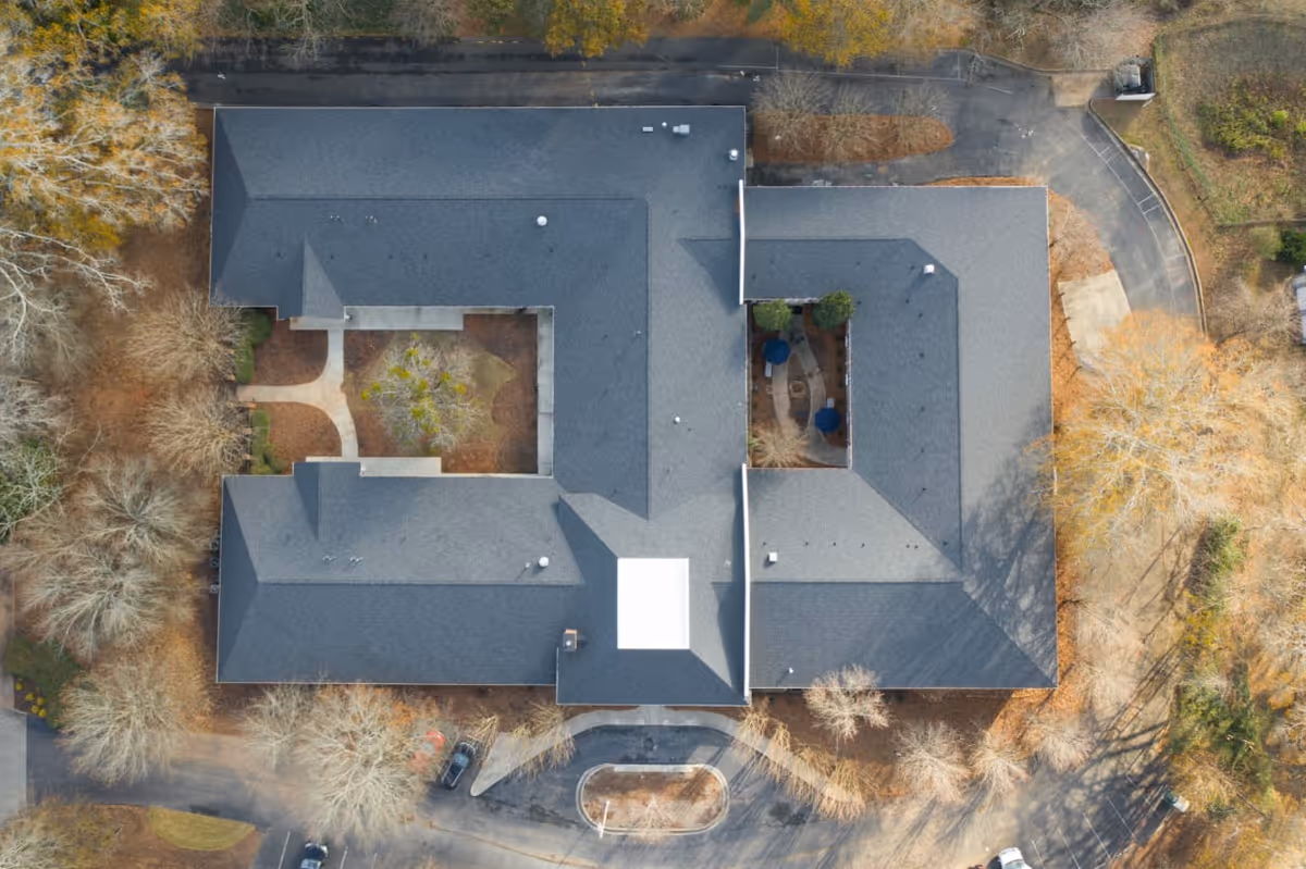Aerial overhead view of a U-shaped senior living facility building with two interior courtyards surrounded by driveways and trees.