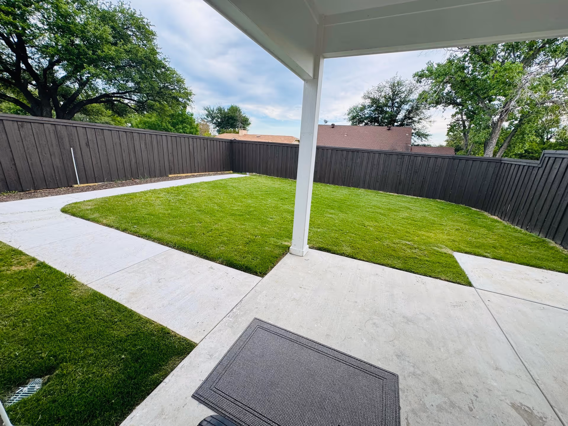 Backyard view with green lawn, concrete pathways, and a covered patio at Orchid Care Homes.
