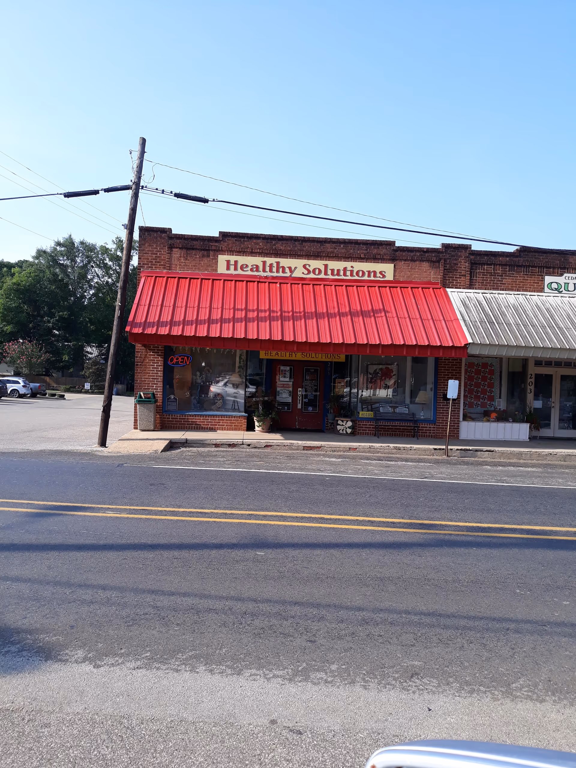 Brick storefront with red awning reading Healthy Solutions on a street.
