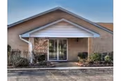 Brick senior living facility entrance with glass doors and landscaped shrubs.