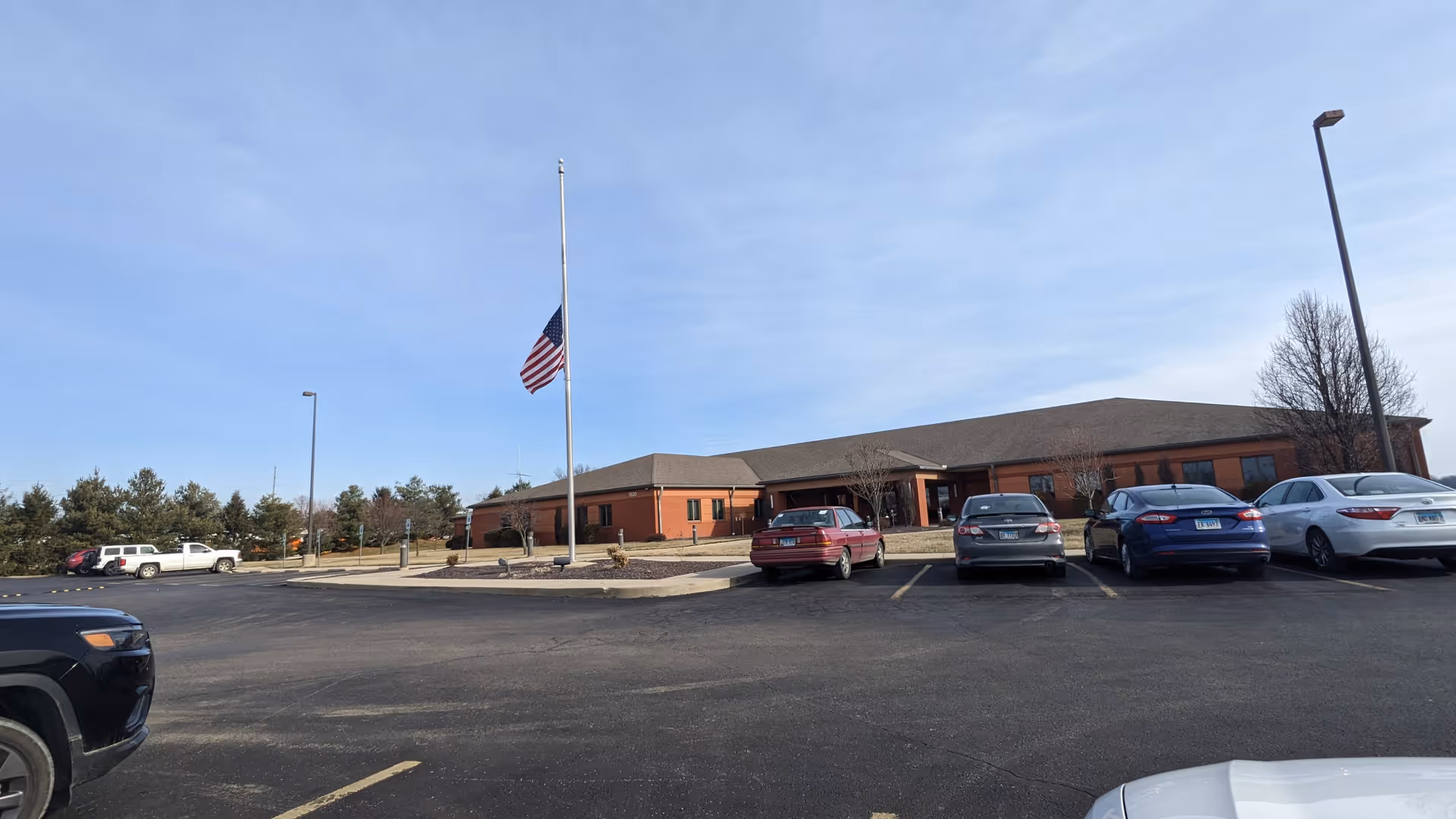 Red brick health department building with a parking lot and an American flag.
