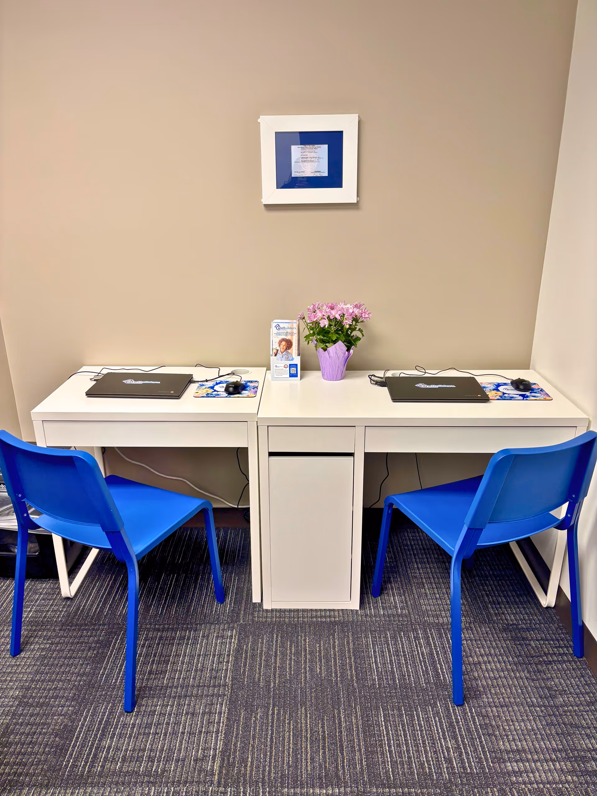 Two white desks with blue chairs facing each other in a small office area.