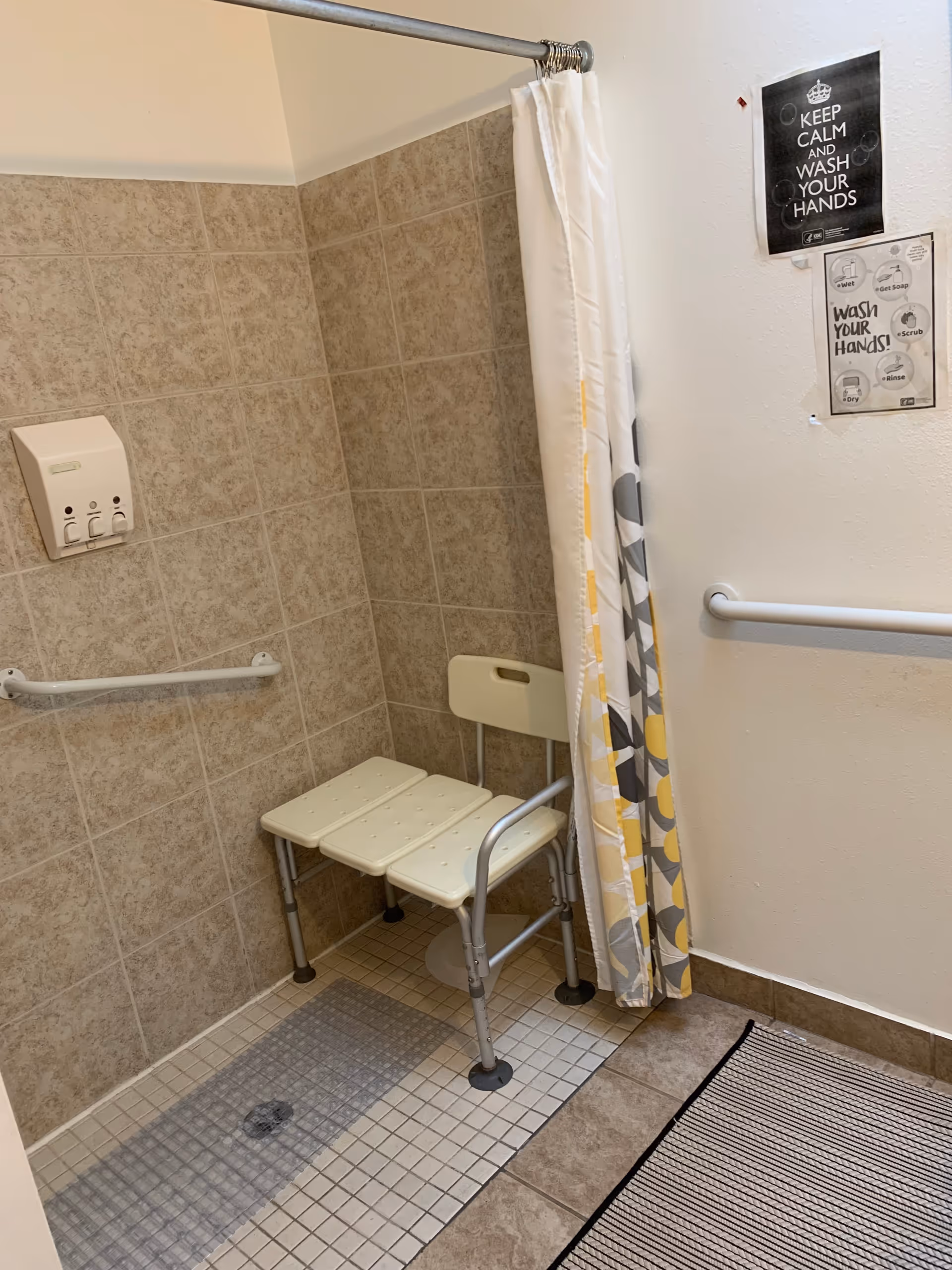 Accessible shower area with a foldable shower chair, grab bars, and a curtain.