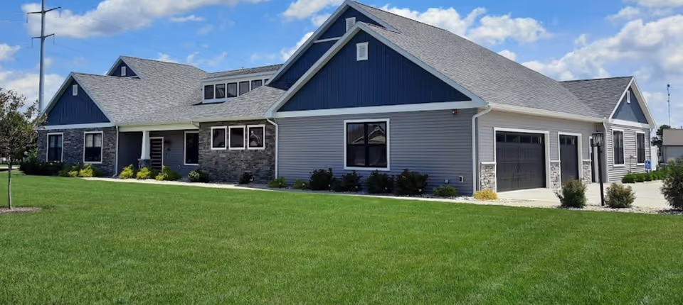 Exterior view of The Laurels of Goshen, blue-gray facility with stone accents and manicured lawn.