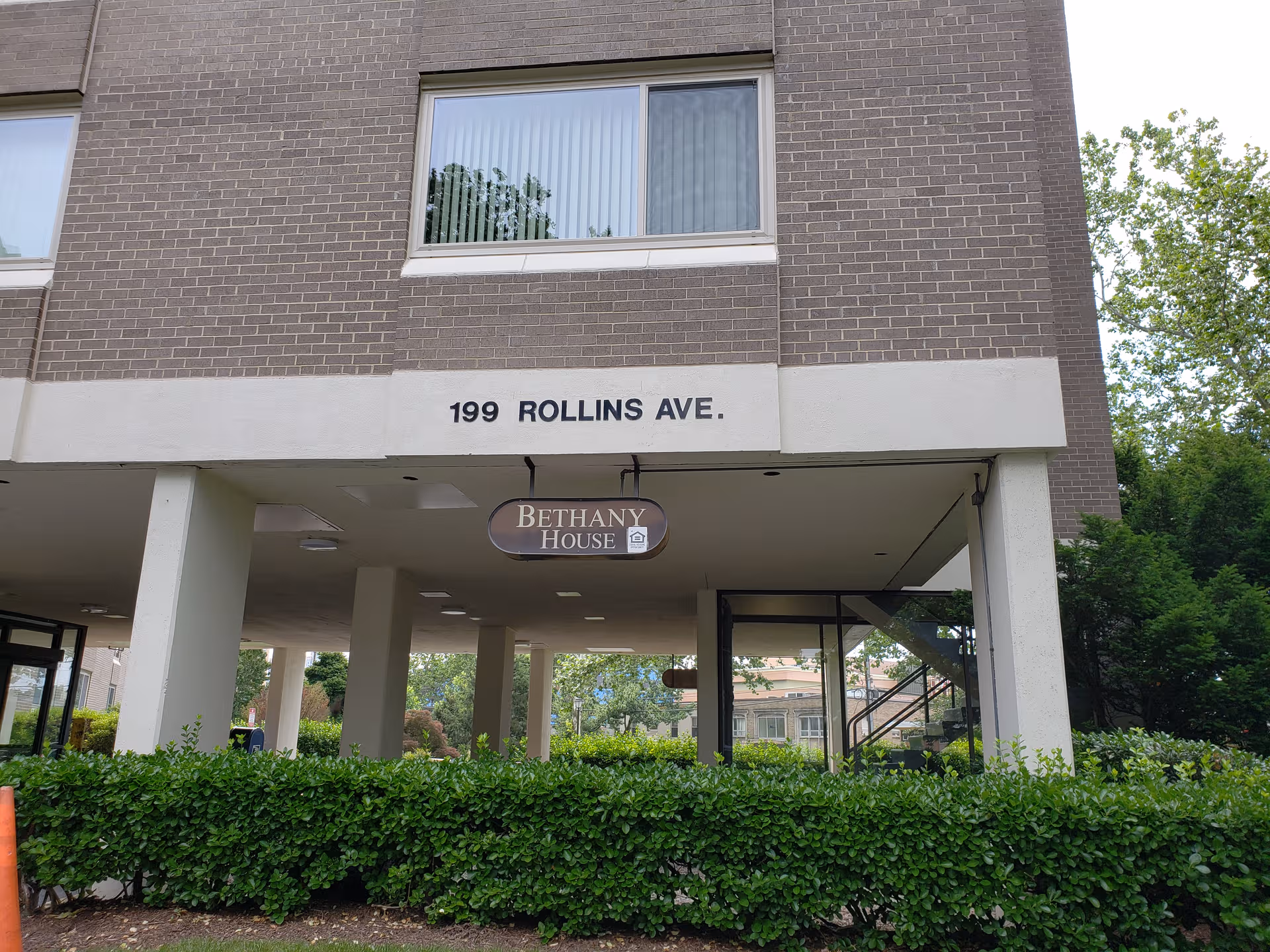 Front view of Bethany House Apartment Building entrance with sign and greenery.