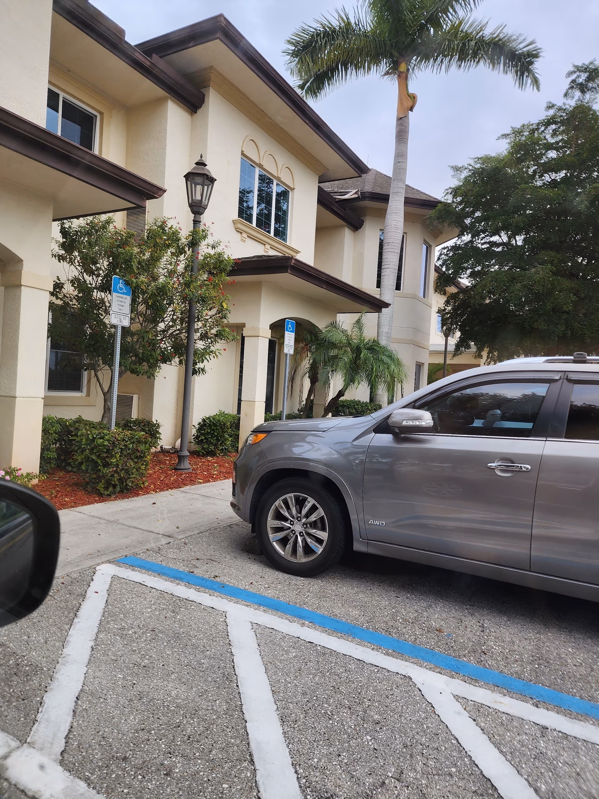 Exterior view of a senior living facility with parked SUV, palm trees, and handicap signs.