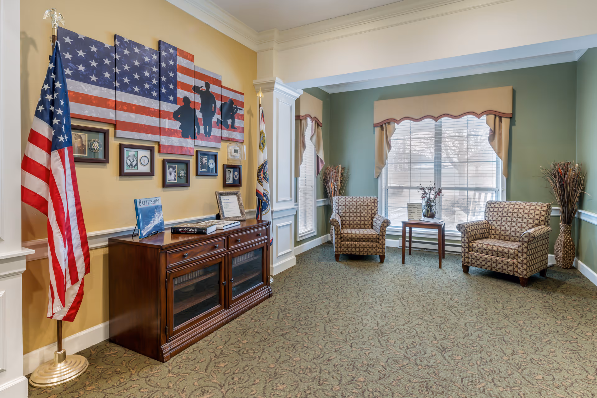 Lobby seating area with two patterned chairs, flags, wall art, and windows.