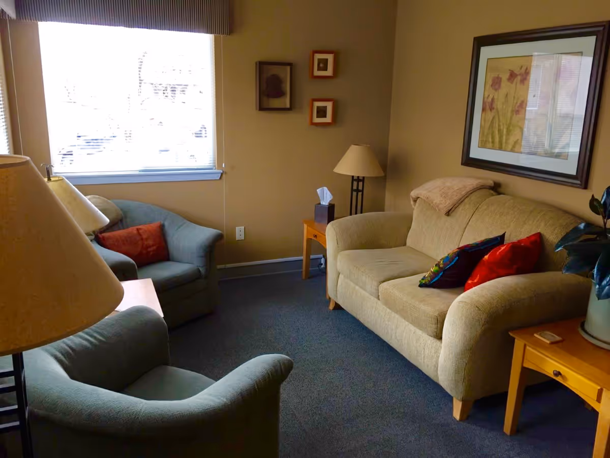 Cozy beige living room with a sofa, armchairs, lamps, and framed wall art.