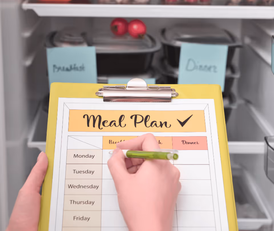 Close-up of a hand writing a meal plan on a clipboard in a dining area.
