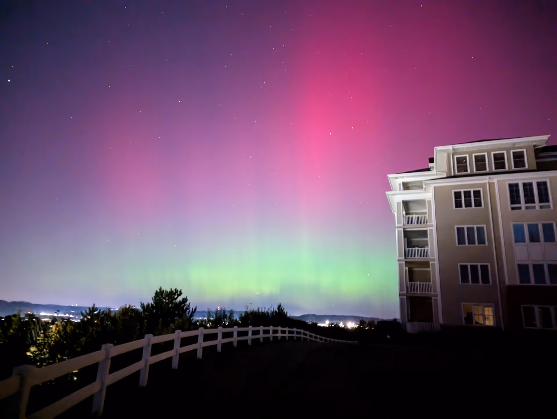 Night exterior of a multi-story retirement building beside a white fence under aurora lights.