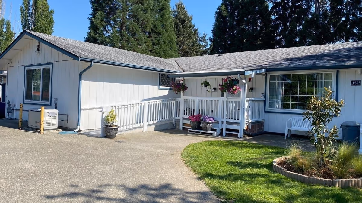 Single-story light-blue senior care building with a small front porch and hanging planters.