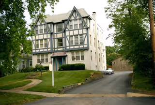 Tudor-style senior living facility exterior with driveway and manicured lawn.