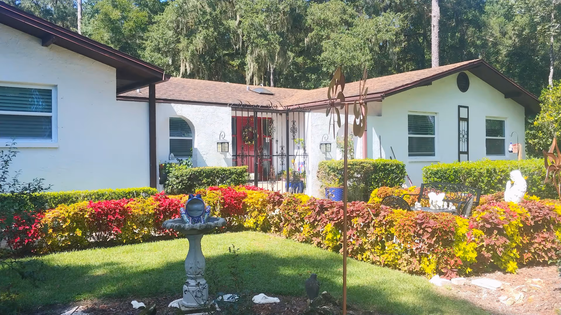 Colorful hedges surround a white single-story senior care home with a decorative fountain.