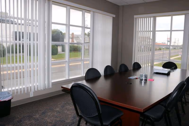Conference room with long table, black chairs, and large windows with vertical blinds.