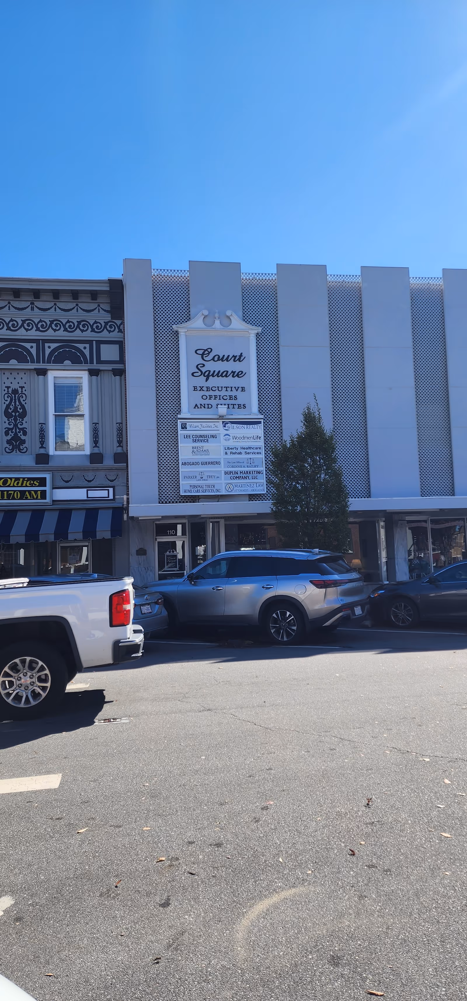 Exterior view of a row of storefronts with a Court Square sign and parked cars