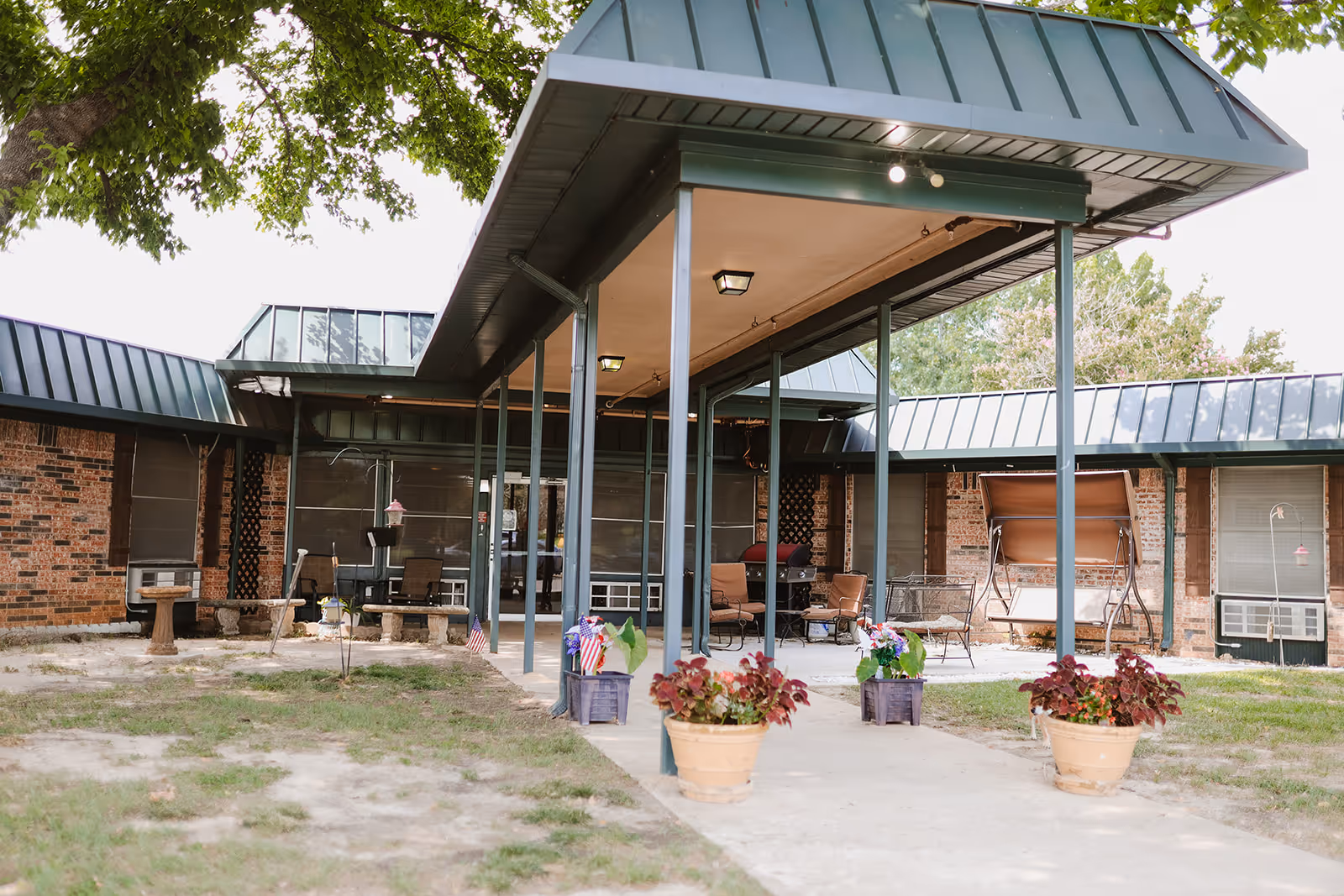 Exterior view of Pecan Creek Healthcare Center showing a covered entrance, brick building, outdoor seating, and flower pots.
