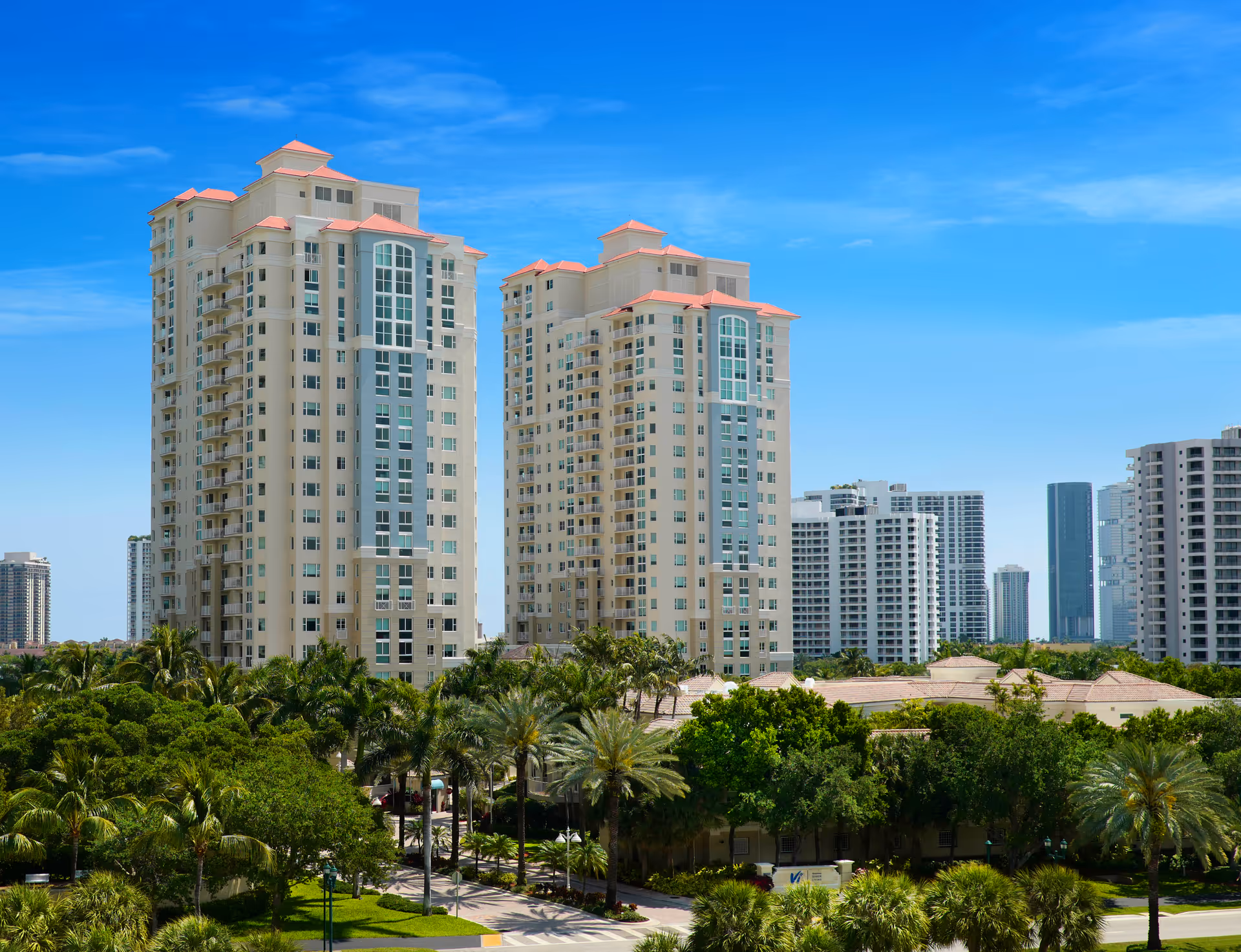 Two beige tall senior living towers with palm trees and a clear blue sky.