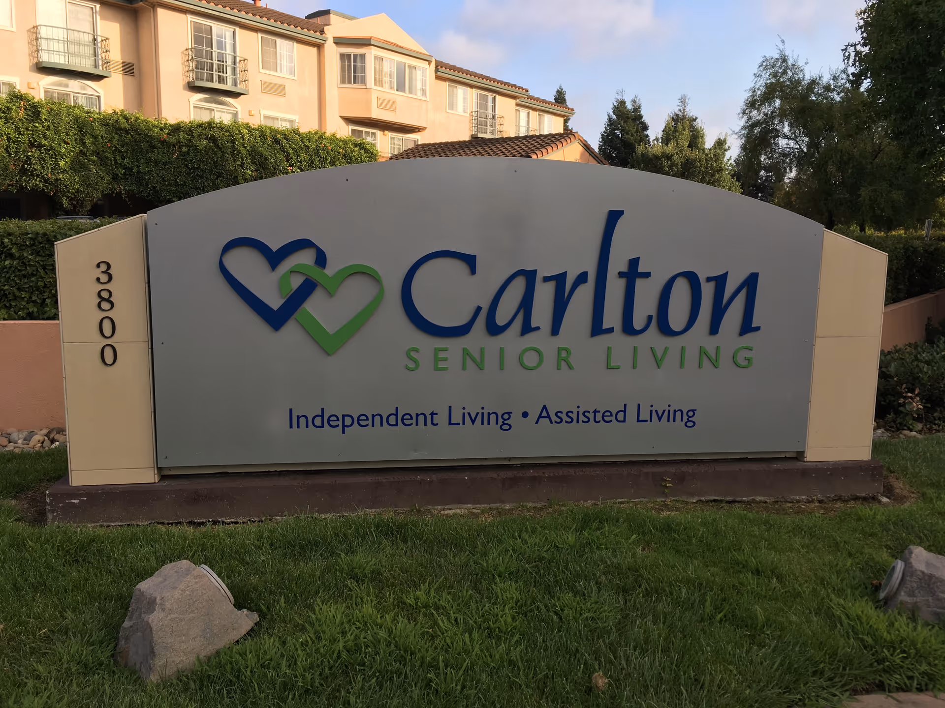 Large Carlton Senior Living sign with green and blue text in front of a beige building.