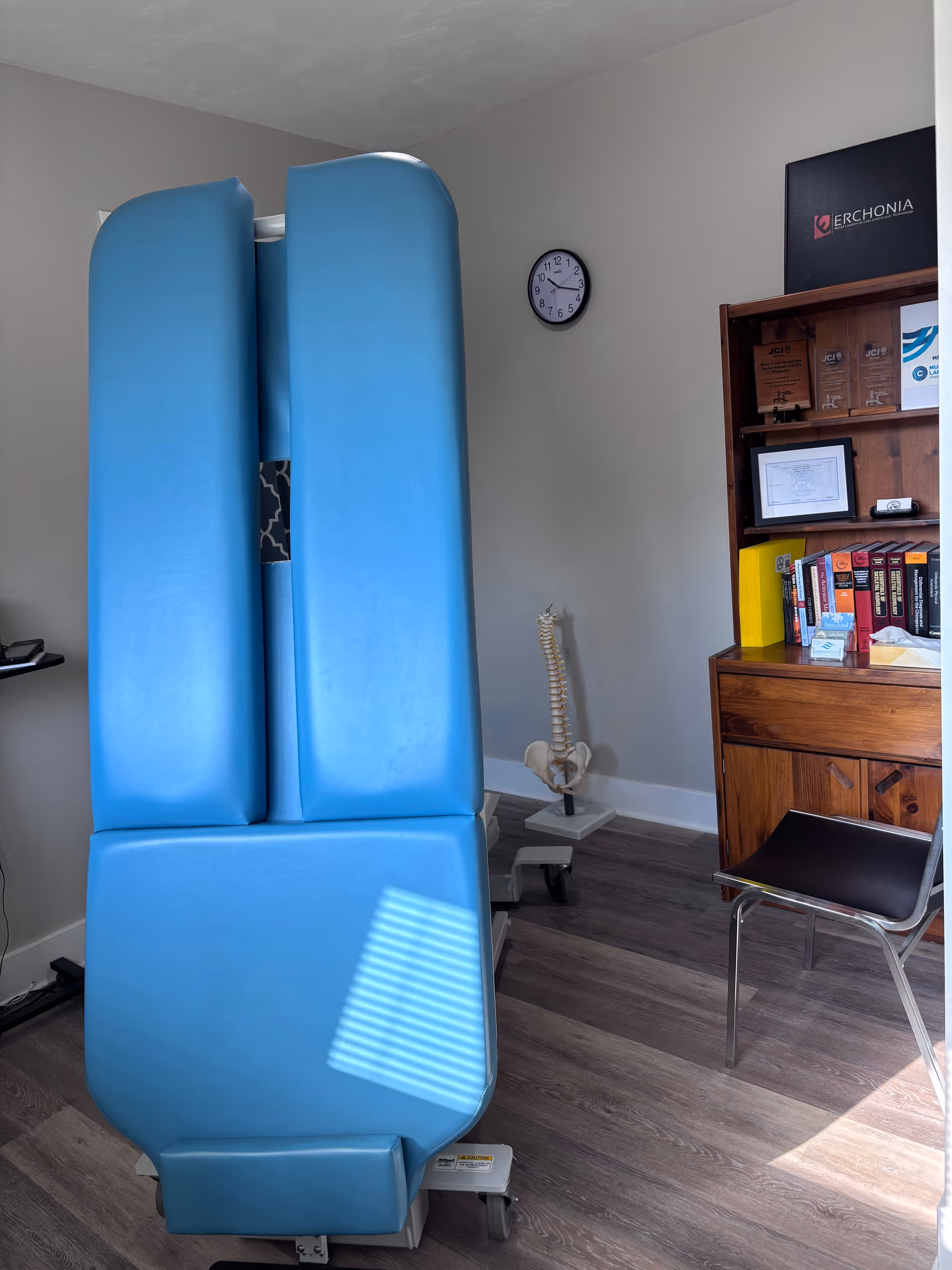 Large blue therapy apparatus beside a spine model in a treatment room.