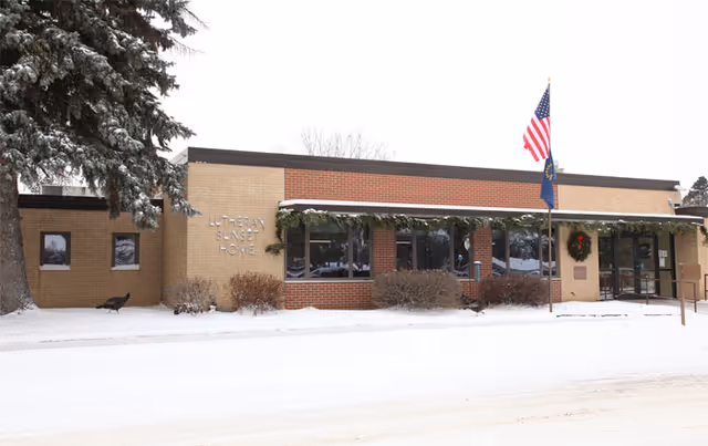 Front exterior of the Lutheran Sunset Home single-story brick building with flags and snow-covered ground.