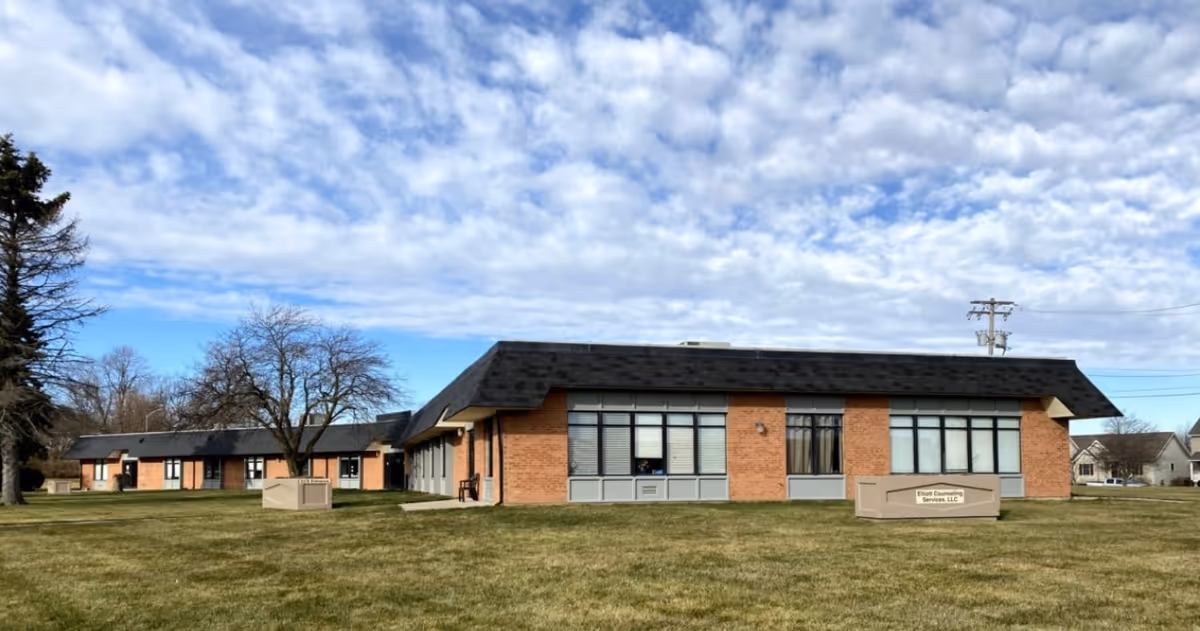 Brick senior care facility exterior with large windows and a grassy front lawn.