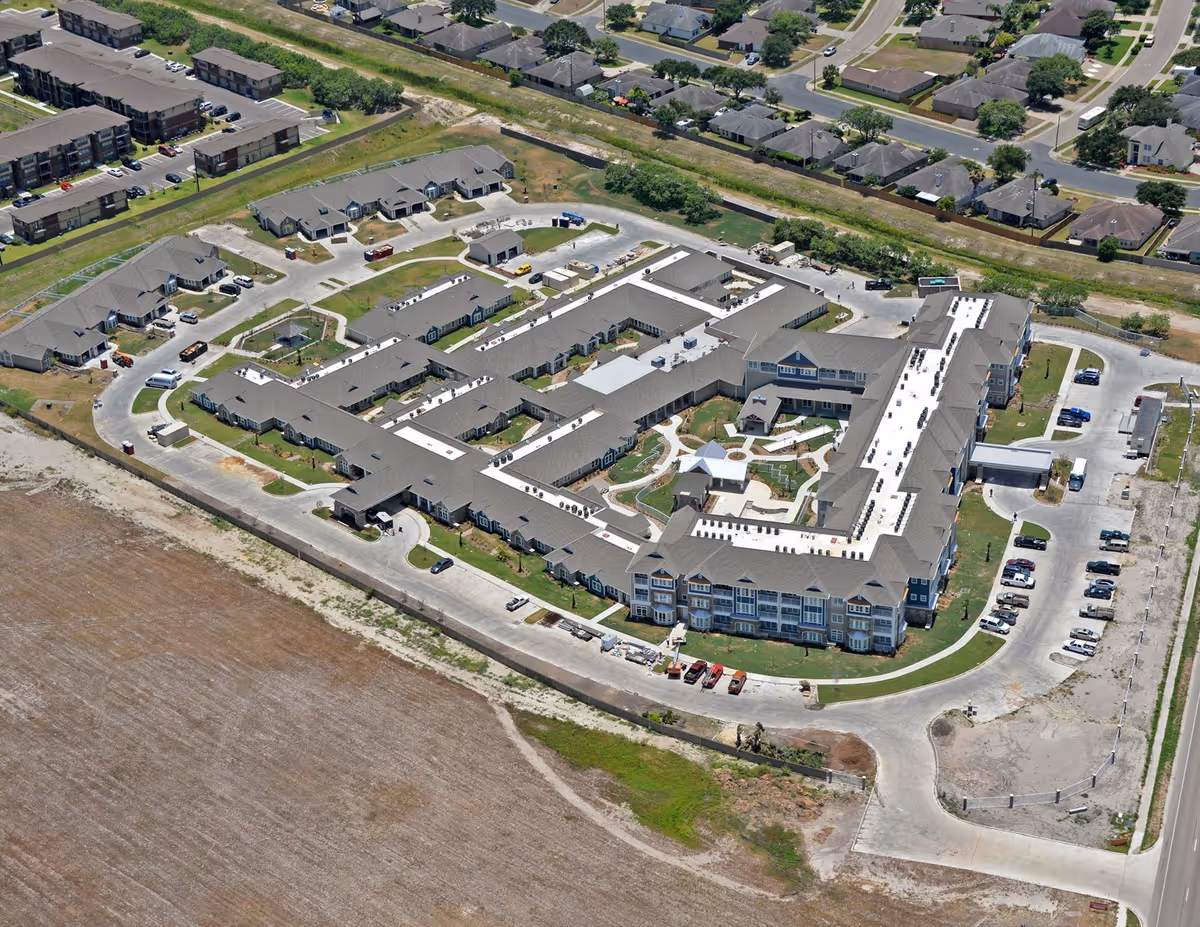 Aerial view of The Viera Senior Living facility showing a large, multi-wing building with a central courtyard, surrounded by parking areas and nearby residential neighborhoods.