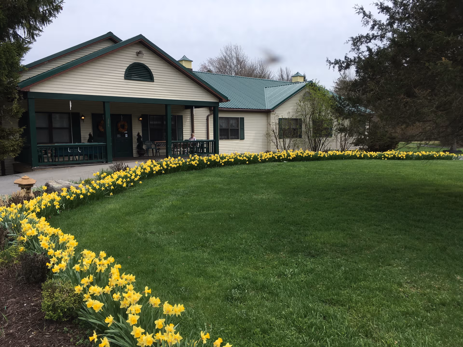 Front view of Twin Cedar Senior Living with yellow daffodils and a green-roofed porch