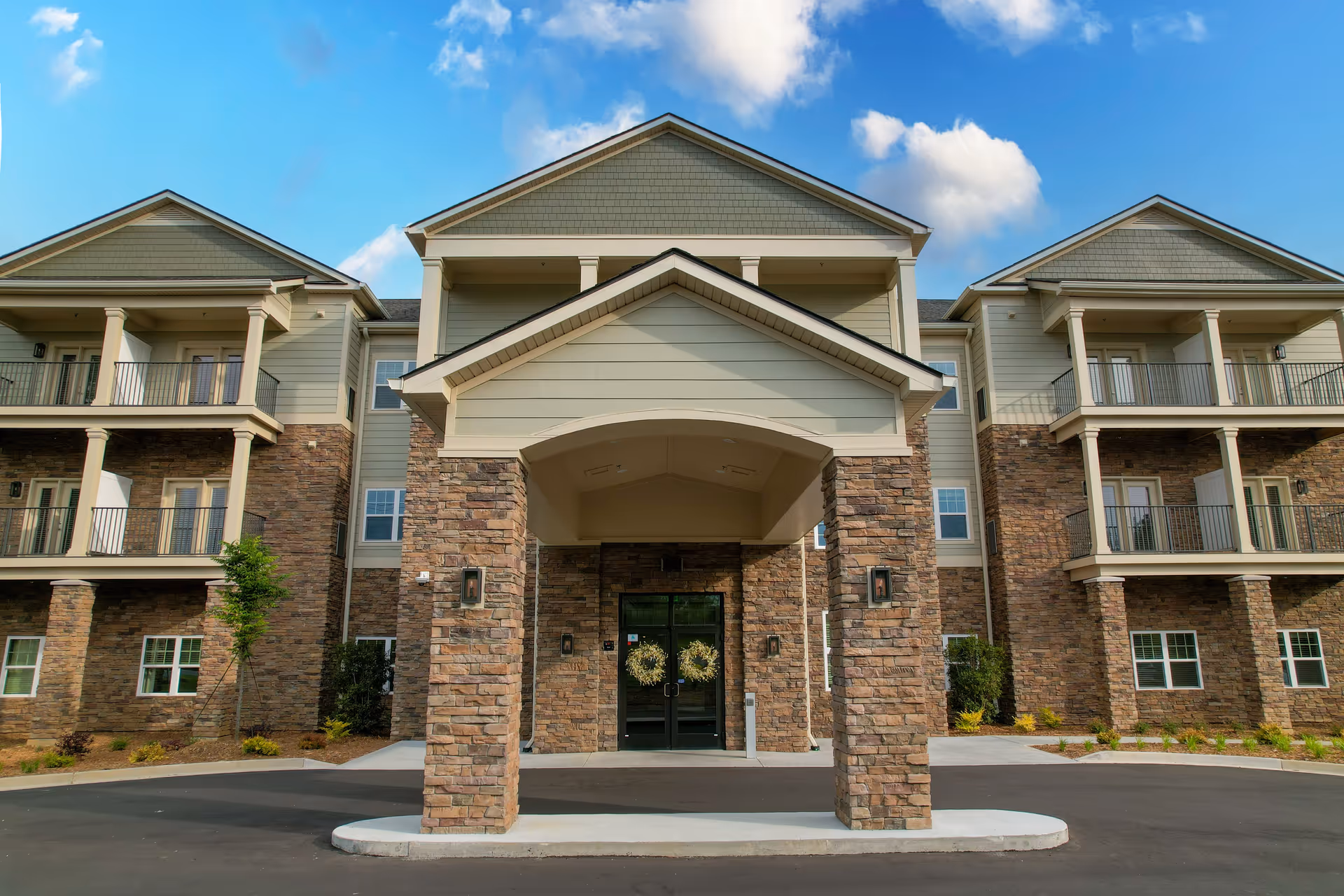 Front entrance of a multi-story senior living building with stone columns and a covered porte-cochère under a blue sky.