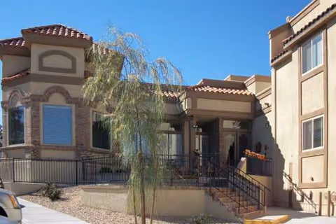 Exterior view of a tan senior living facility with stairs and desert landscaping.
