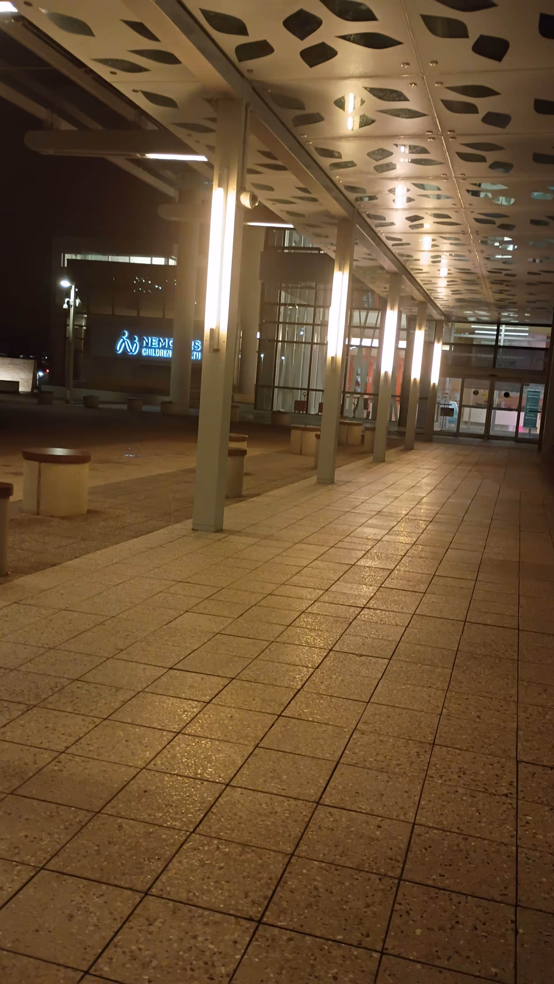 Night view of a covered outdoor walkway with columns leading to a hospital entrance.