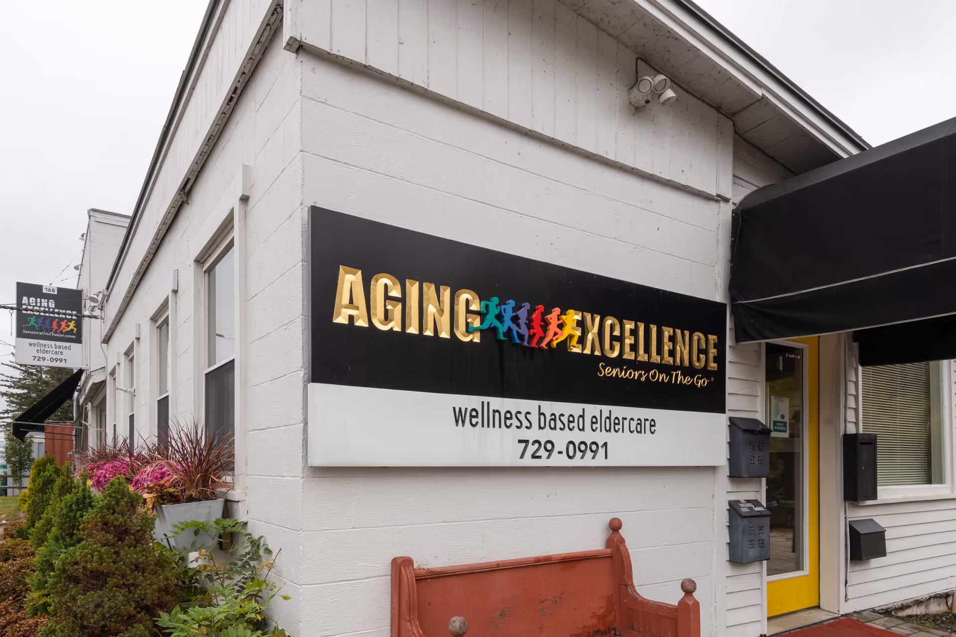 Aging Excellence sign on a white building exterior with a yellow door.
