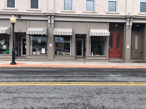 Exterior storefront with striped awnings and a red door along the street.