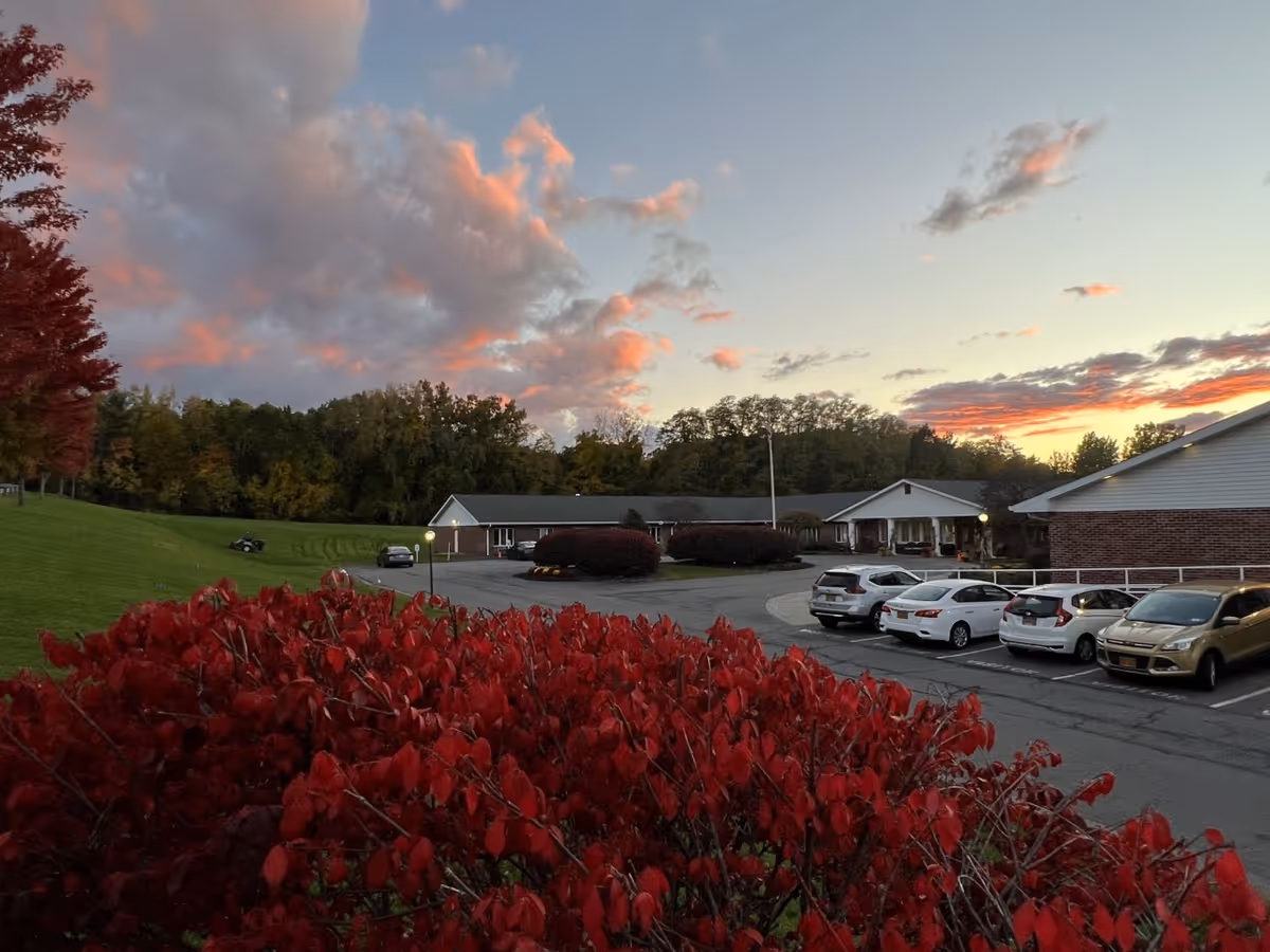 Sunset over Elderwood Village at Colonie exterior with red bushes and parked cars