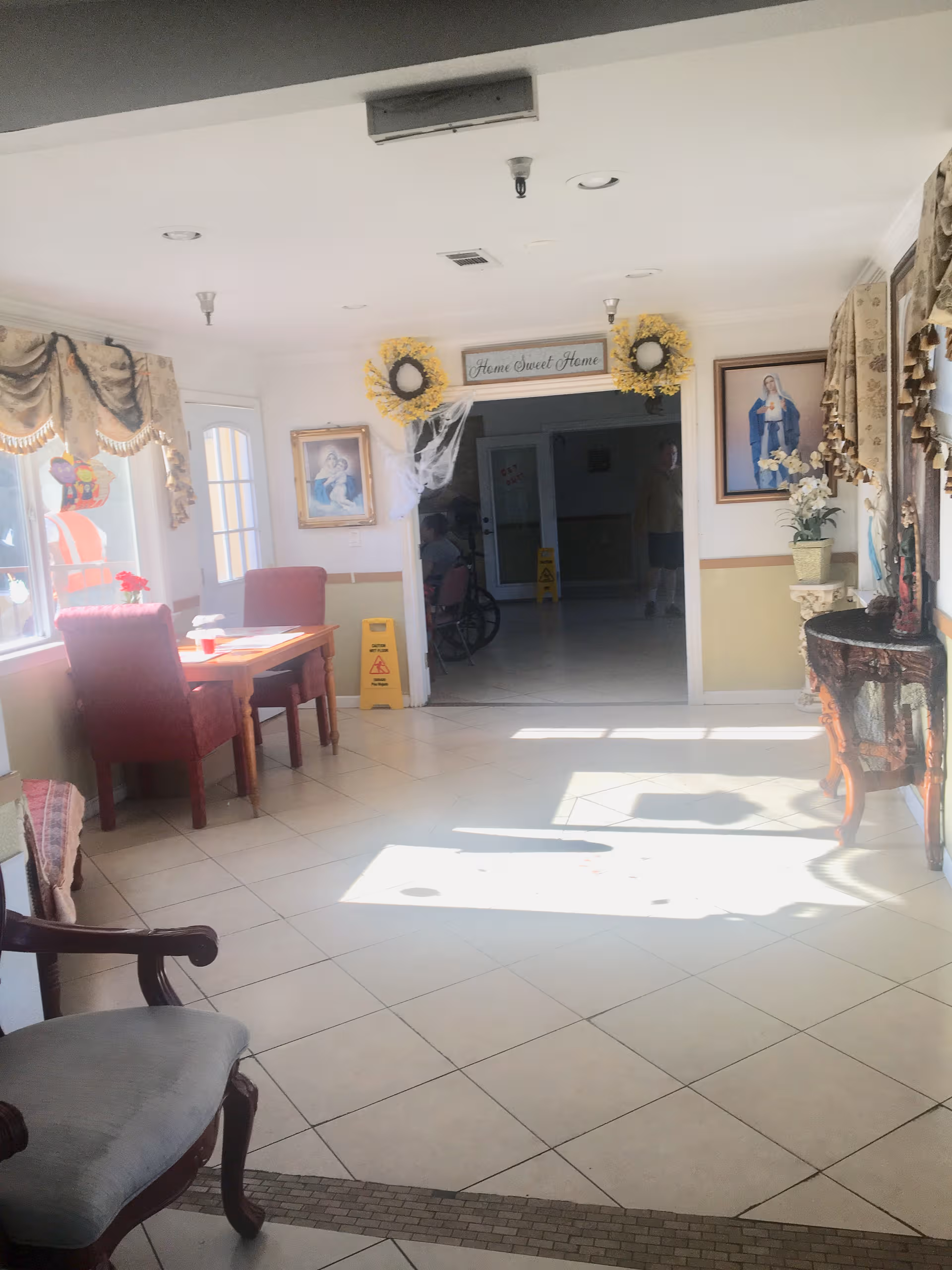 Bright senior living lobby with seating, draped decor, and a doorway reading 'Home Sweet Home'.