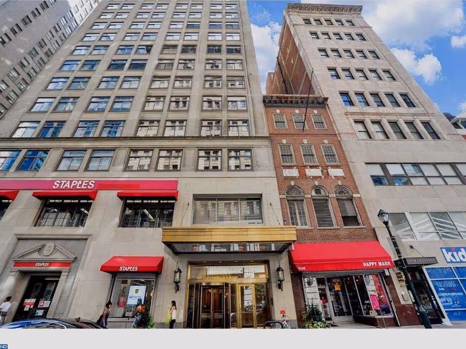 Tall city buildings line a busy street with Staples storefronts and colorful awnings.
