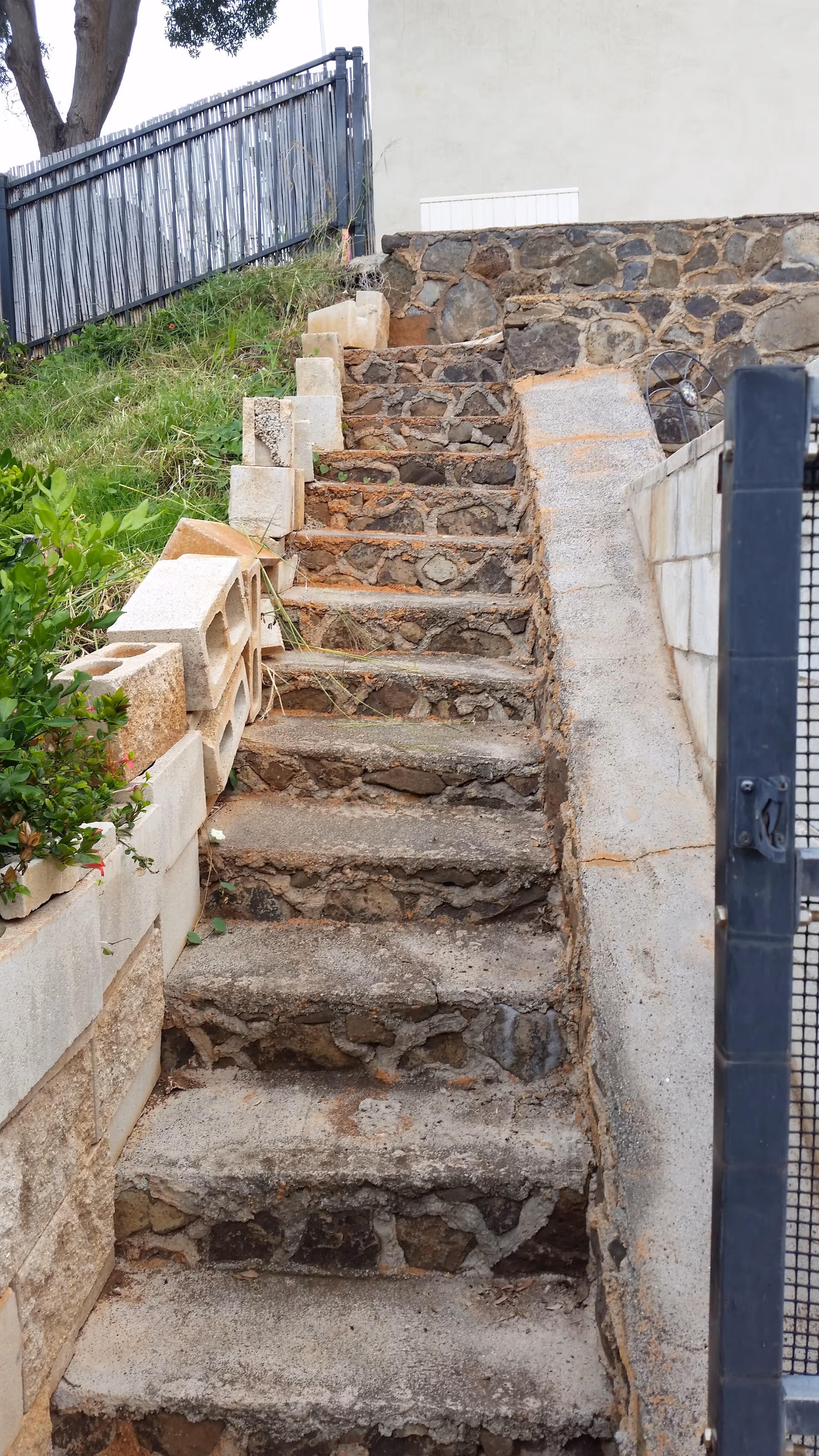 Outdoor stone stairs along a retaining wall beside a building, with blocks and greenery.