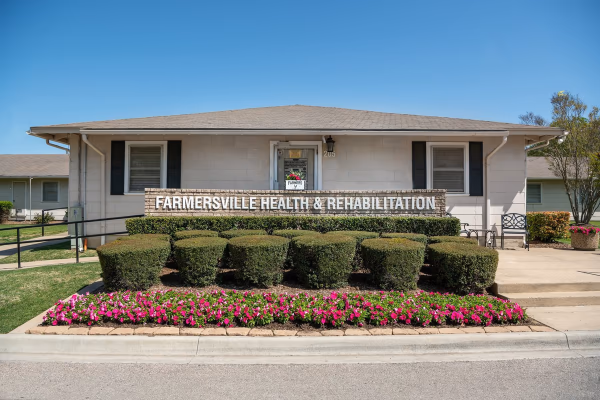 Front view of Farmersville Health and Rehabilitation building with hedges and pink flowers.