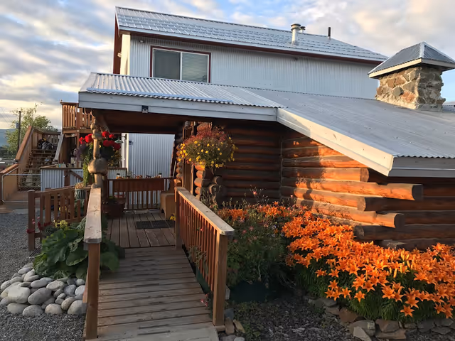 Exterior view of a rustic facility entrance with a wooden deck, ramp, and orange flowers.