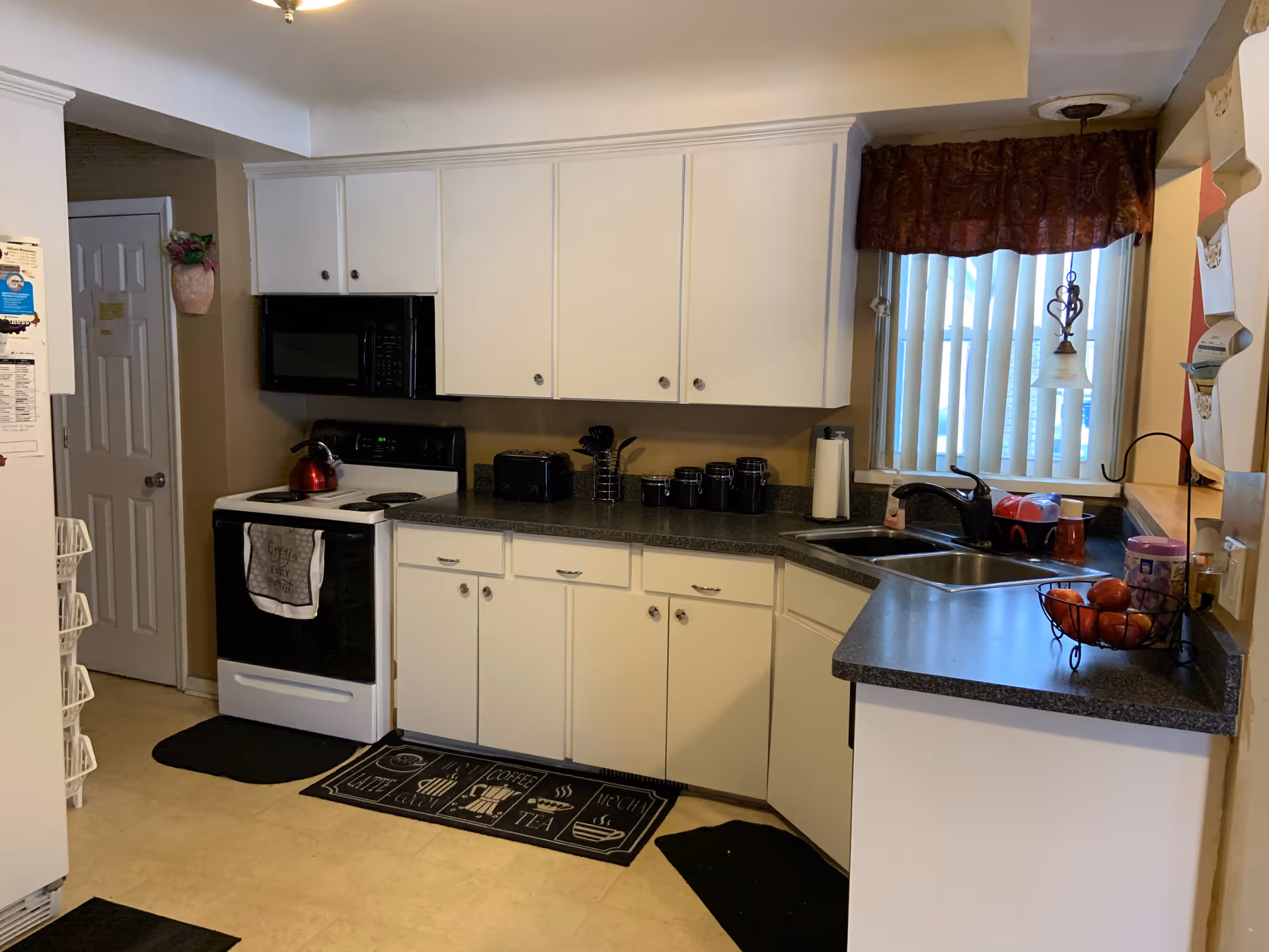 Bright white Arbor Manor kitchen with cabinets, appliances, and window blinds.