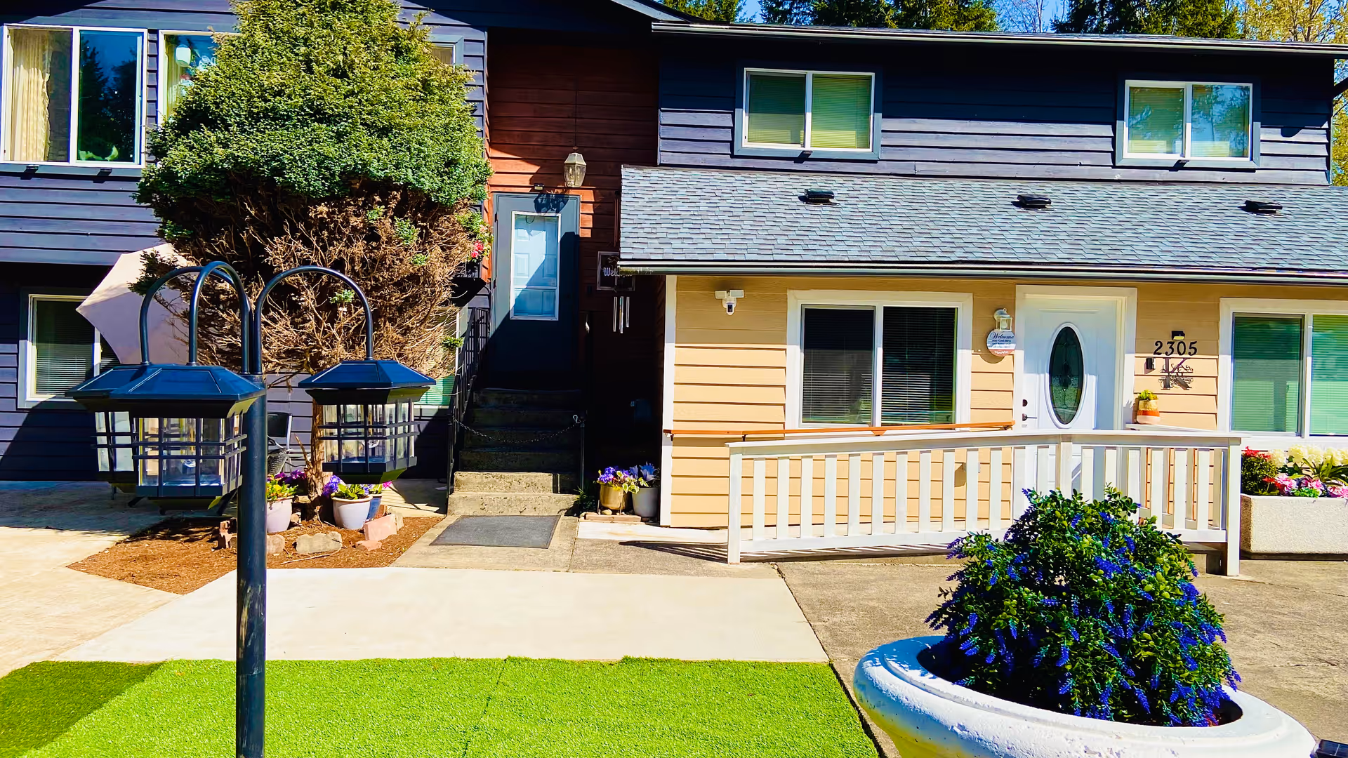 Front exterior of a two-story senior living facility with a porch and landscaped yard.