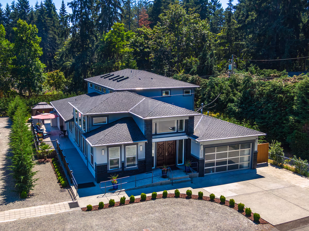 A modern blue two-story senior living home with a paved driveway and landscaped front.