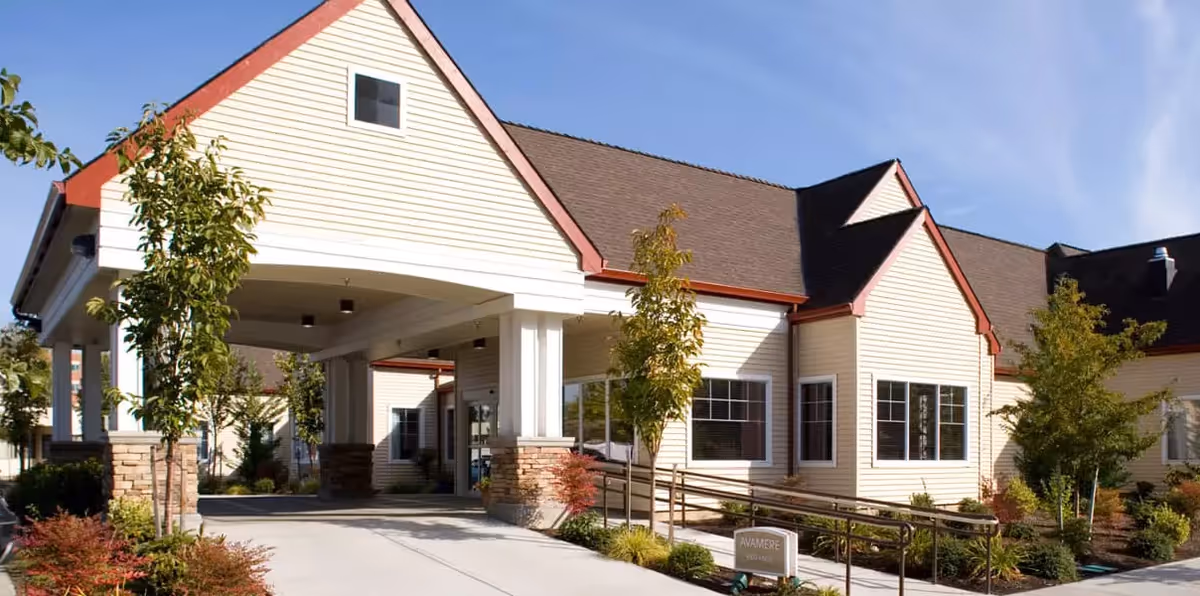 Single-story senior living facility exterior with covered entrance, columns, and landscaped path.