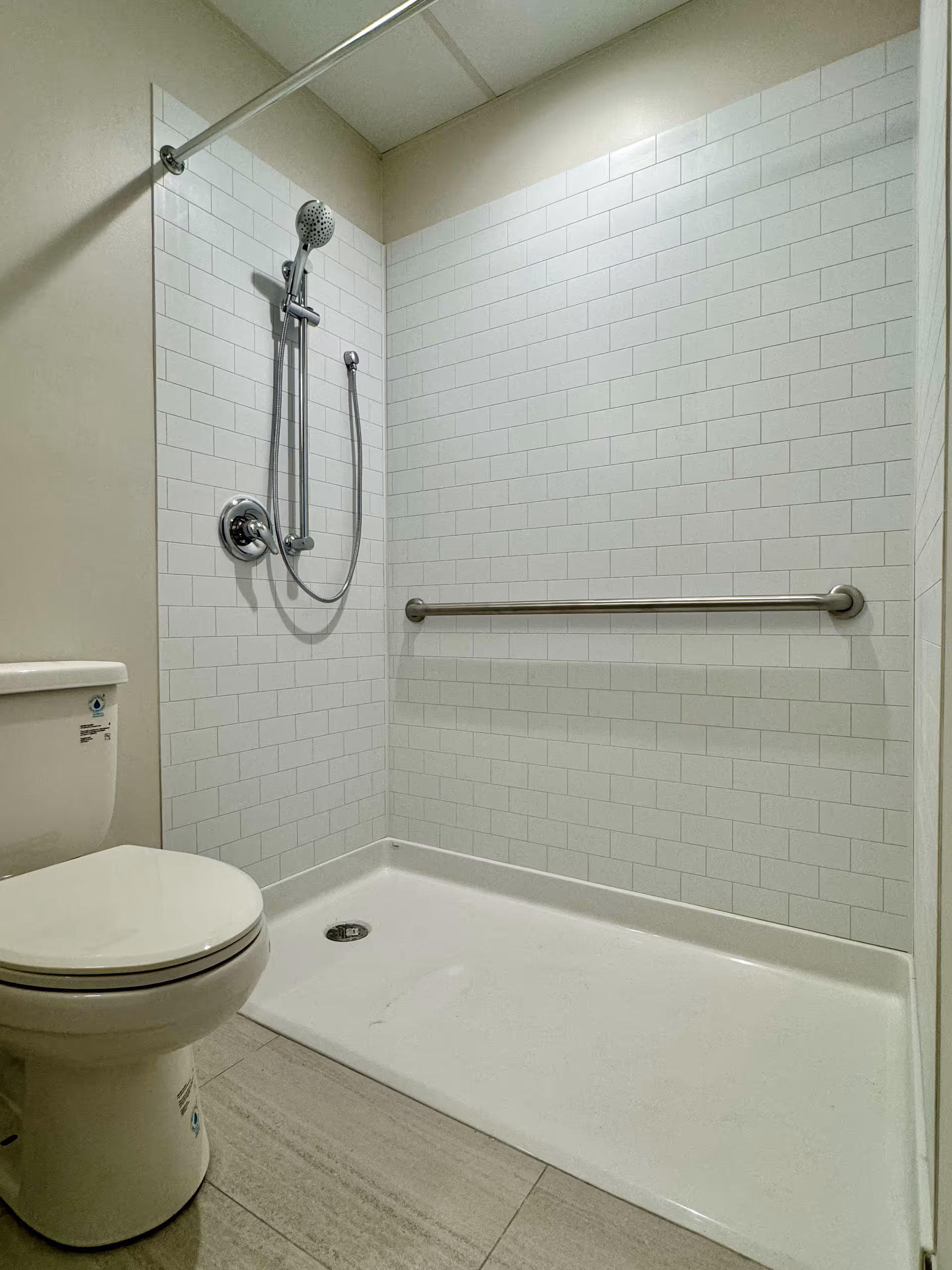 Accessible bathroom with a shower, grab bar, and toilet in a tiled room.