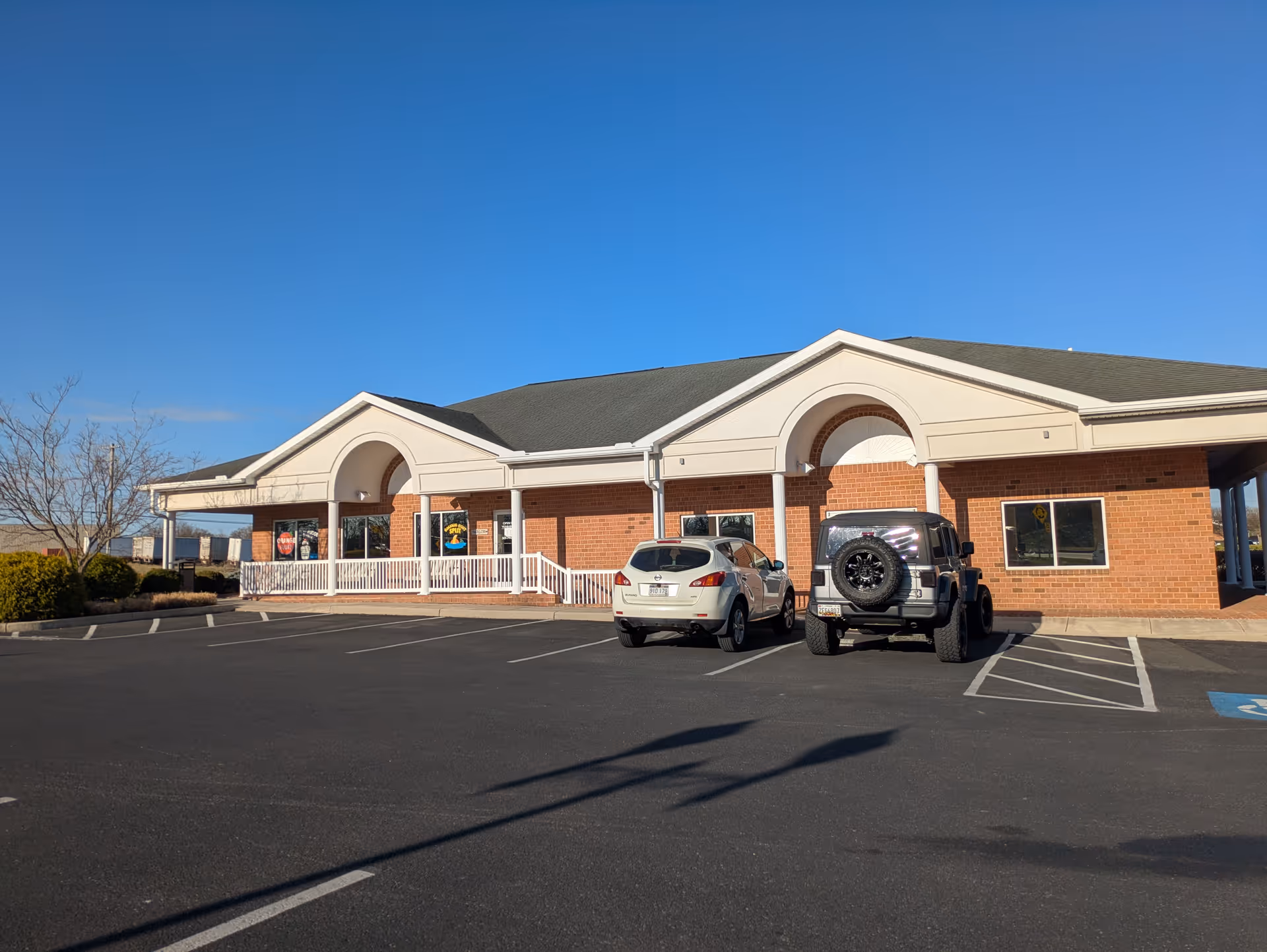 Brick, single-story building with arched entryways and a parking lot in front.