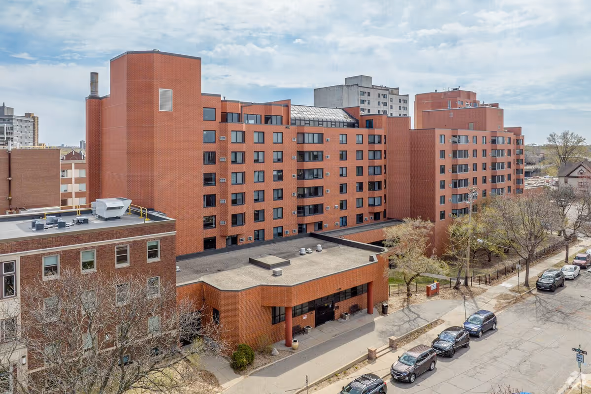 Exterior view of Runnstone Senior Living, a red brick multi-story building with street and parked cars.