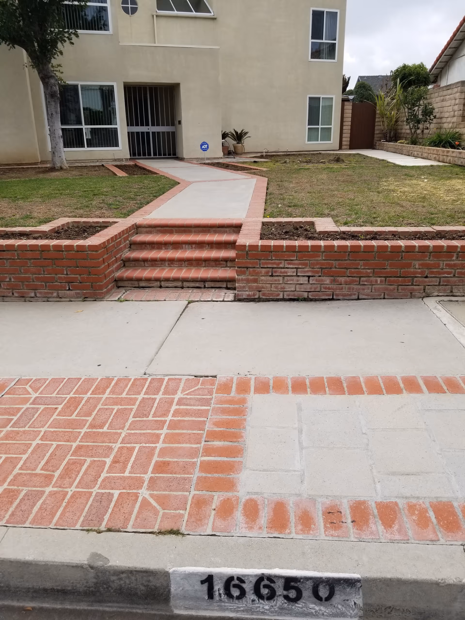 Front exterior entrance of a beige senior living building with brick walkway and steps.